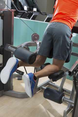 Kneeling leg femoral curl man exercise at gym rear view workout